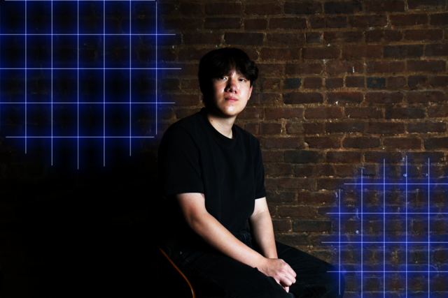A young man in a black shirt sits against a brick wall with blue glowing grid patterns on the left and right sides.